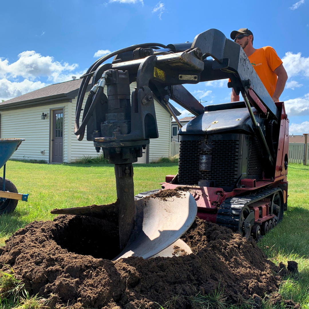 Closeup of an itrees.com crew member using a piece of equipment called a Toro Dingo showing its giant drill-bit like attachment digging a hold for tree planting.