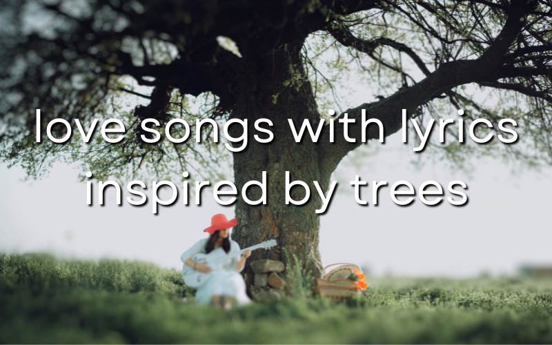 A woman in a peach colored hat and a white dress playing acoustic guitar under a tree