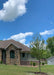 A newly planted Burgundy Belle stands with green leaves in the front yard of a new construction home. 